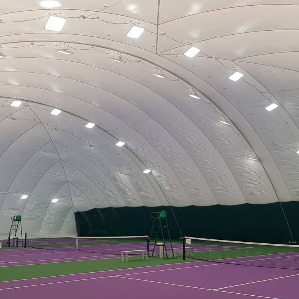 Indoor tennis court in an inflatable dome with a purple surface, lighting fixtures on the ceiling, and green boundary lines.