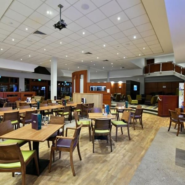 Dining area at DL Northwood Gallery with wooden tables and green-cushioned chairs under ceiling lights, and wooden accents throughout.