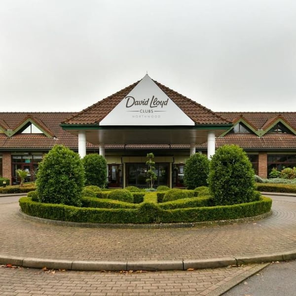 Exterior of David Lloyd Northwood Club with manicured hedges, a triangular roof, and flag poles.