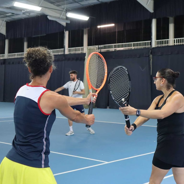 Tennis players during a training session at David Lloyd Southampton, guided by a coach on an indoor court.