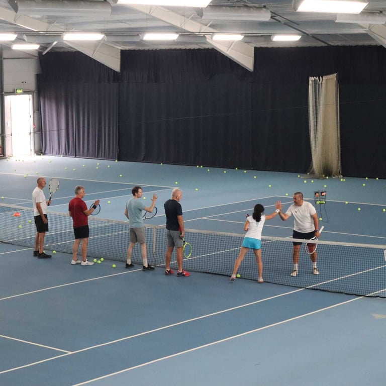 Adults playing tennis indoors at David Lloyd Southampton, engaging in a high-five over the net during a lesson.