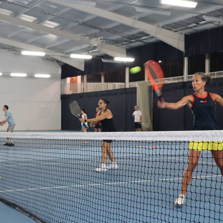Indoor tennis court at DL Southampton with players in a doubles match, focused on hitting the ball with forehand strokes.