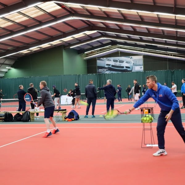 Indoor tennis coaching session with instructor guiding players on a court.