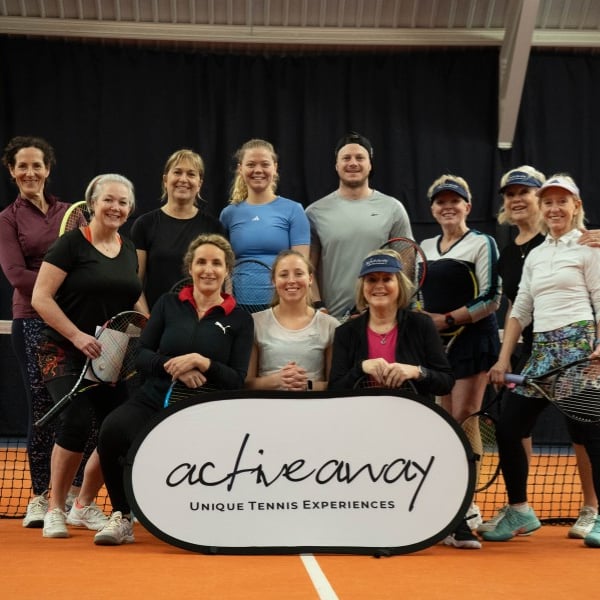 Group of tennis players on indoor court with Active Away sign, featuring nine women and one man holding tennis racquets.