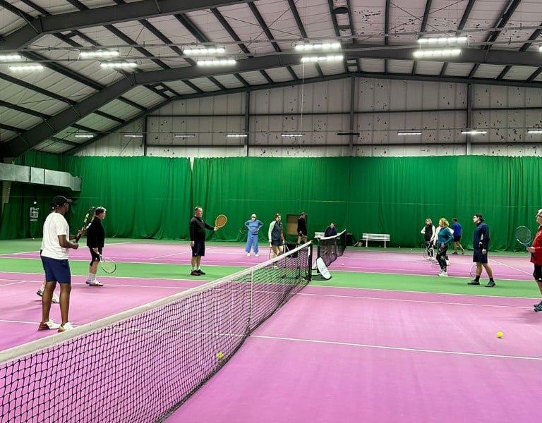 Indoor tennis coaching session with players on a pink court at DL Woking sports facility.