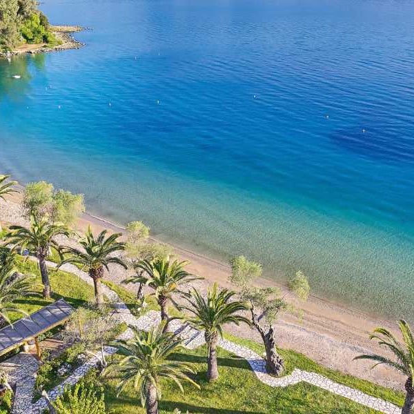 Aerial view of Daphnila Bay featuring a beachfront with palm trees and clear turquoise waters, with a docked boat visible.