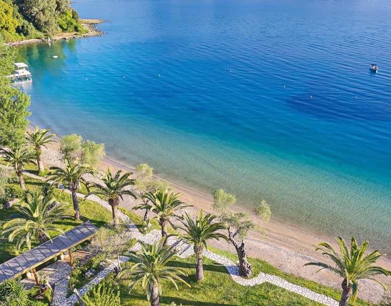 Aerial view of Daphnila Bay featuring a beachfront with palm trees and clear turquoise waters, with a docked boat visible.