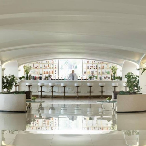 Daphnila Bay Bar with a modern white design, curved ceilings, well-stocked shelves, bar stools, and potted plants.
