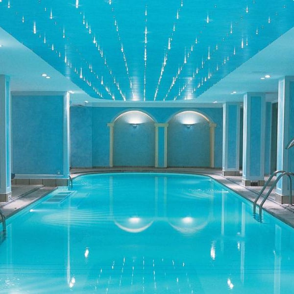 Indoor swimming pool at Daphnila Bay spa with blue walls, ceiling lights, and entry steps.