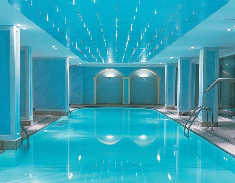 Indoor swimming pool at Daphnila Bay spa with blue walls, ceiling lights, and entry steps.
