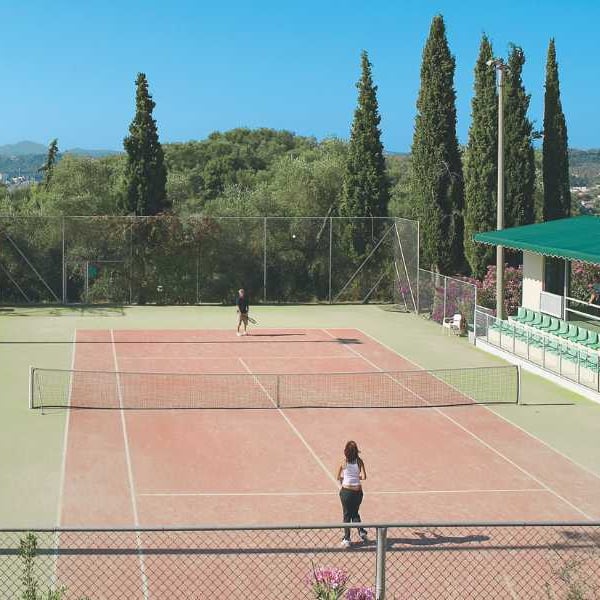 Tennis courts at Daphnila Bay with players, surrounded by greenery, cypress trees, and hills in the background.