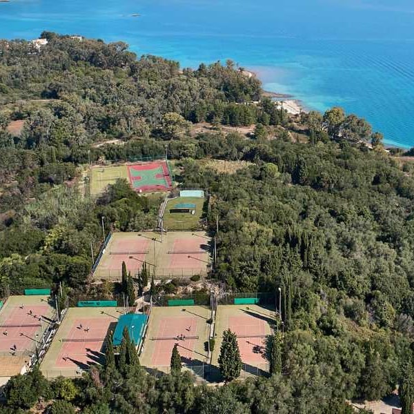 Aerial view of tennis courts surrounded by greenery near the waters of Daphnila Bay.