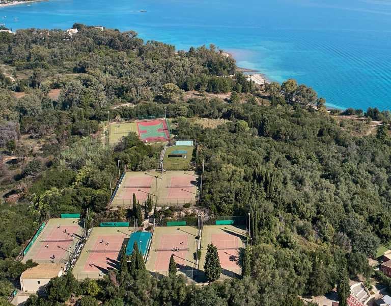 Aerial view of tennis courts surrounded by greenery near the waters of Daphnila Bay.