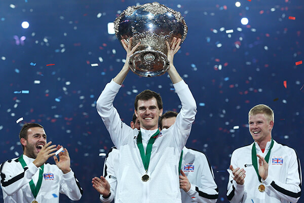 Jamie Murray holding the Davis Cup trophy, surrounded by celebrating Great Britain team members and falling confetti.