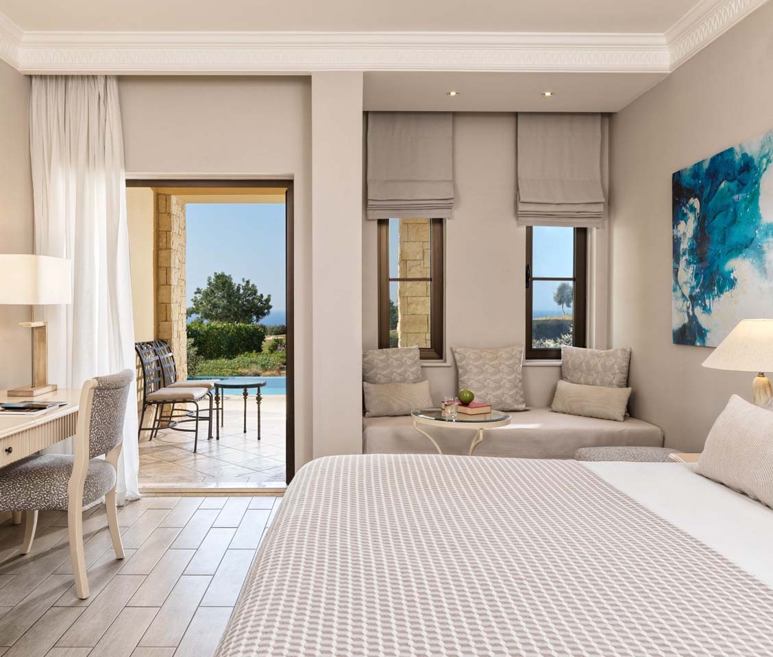 Luxurious hotel room with a double bed, lounge area, and desk, offering private terrace access with pool, golf, and sea views.