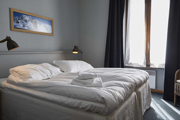 Interior of a double twin room at Hotel Monterosa with two single beds, white bedding, reading lamps, and a mountain photo on the wall.