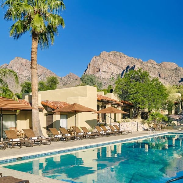El Conquistador Resort pool area with sun loungers and parasols, set against a backdrop of mountains and clear skies.