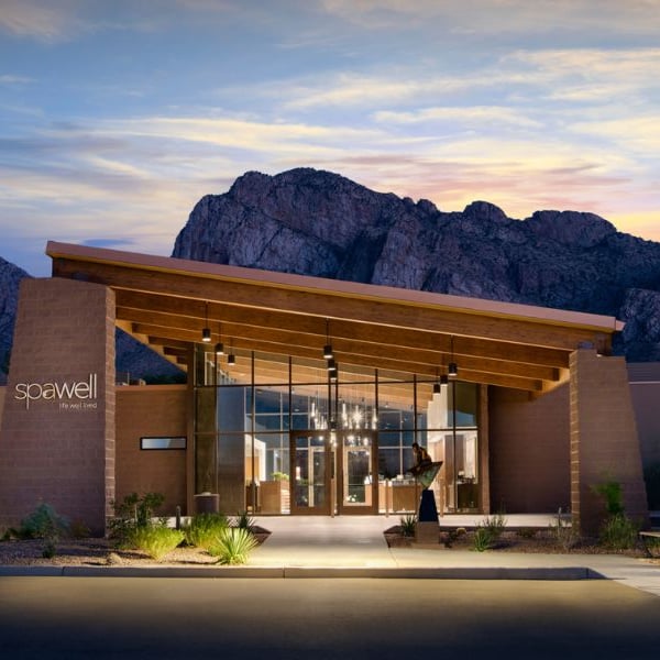 Exterior view of El Conquistador Gallery spa with mountains at sunset, highlighting modern architecture with glass and wood elements.