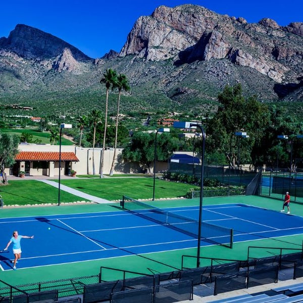 Tennis court at El Conquistador Gallery with players and mountain backdrop under a clear sky.