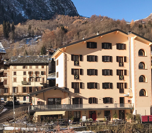 Exterior view of Cristallo Hotel with cream facade and wooden shutters, set against snow-capped hills and autumn trees.