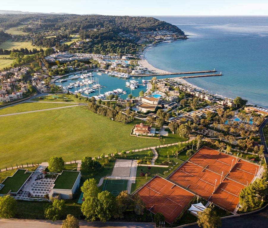 Aerial view of Sani Beach resort in Greece, featuring tennis courts, a marina with yachts, and a beach along the Aegean Sea.