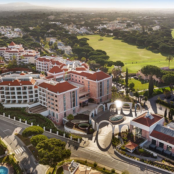 Aerial view of Hilton Vilamoura As Cascatas Golf Resort & Spa, surrounded by golf courses and greenery under a clear sky.