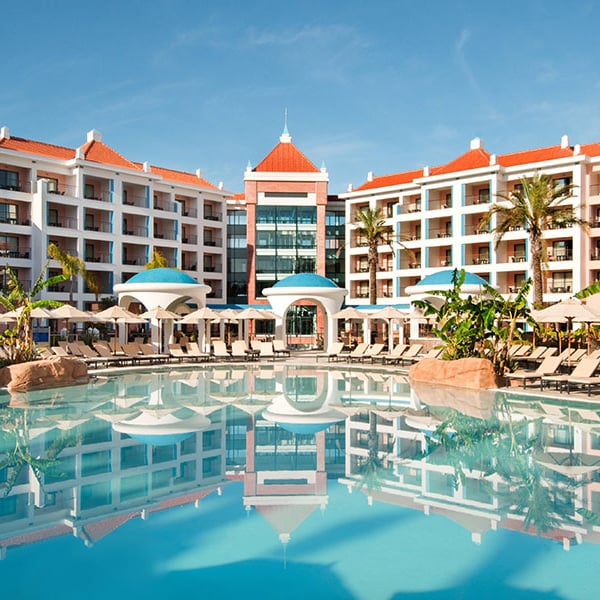 Exterior view of Hilton Vilamoura resort in Portugal, showcasing the central pool, sun loungers, tropical plants, and grand architectural design.
