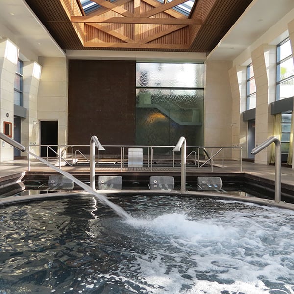 Indoor spa pool at Hilton Vilamoura with jets, wooden beams, and large windows letting in natural light.