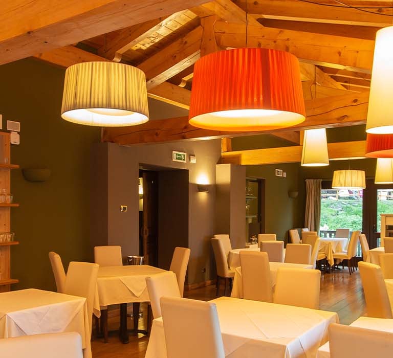 Interior of Hotel Cristallo restaurant with white tablecloths, coloured pendant lamps, and wooden decor.