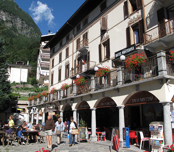 Hotel Monterosa building with balconies, red flowers, and outdoor seating at Bar La Moccetteria in an alpine village.