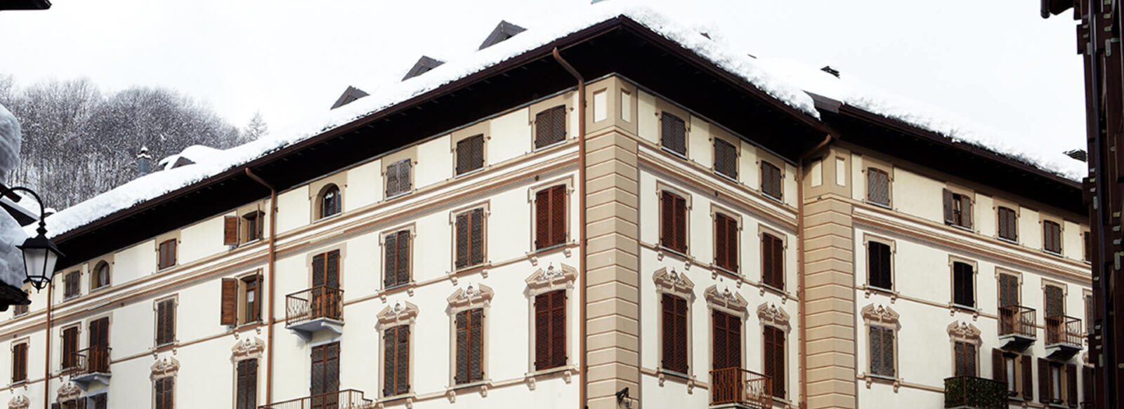 Exterior view of Hotel Monterosa, showcasing classic architecture with wooden shuttered windows and snow-covered mountain scenery.