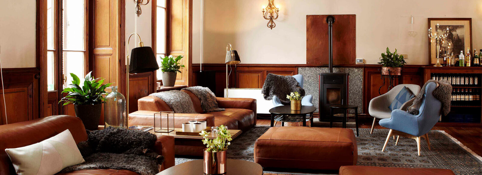 Luxurious hotel lounge with leather sofas, armchairs, plants, vintage lighting, and a bookshelf in a wood-finished interior.