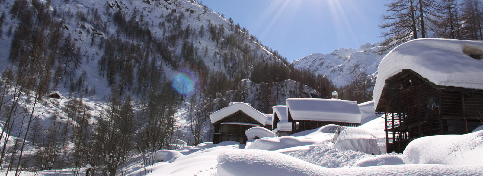 Snow-covered wooden cabins at Hotel Monterosa, surrounded by the Swiss Alps under a bright blue sky.