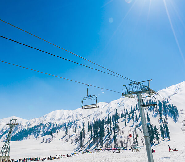Ski lift against a backdrop of snow-covered mountains and pine trees under a bright blue sky near Hotel Monterosa.