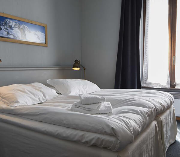 Hotel Monterosa room with a double bed, white linens, folded towels, a bedside lamp, and a mountain landscape picture above the bed.