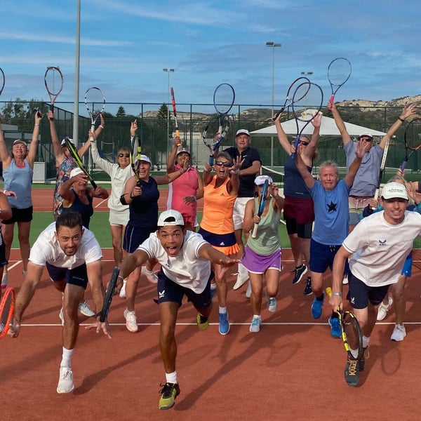 Group of tennis players on a clay court holding rackets up, depicting excitement and energy.