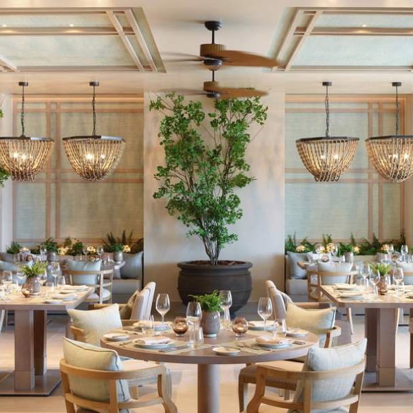 Elegant dining area at Ikos Aria with chandeliers, plants, and neatly arranged tables.