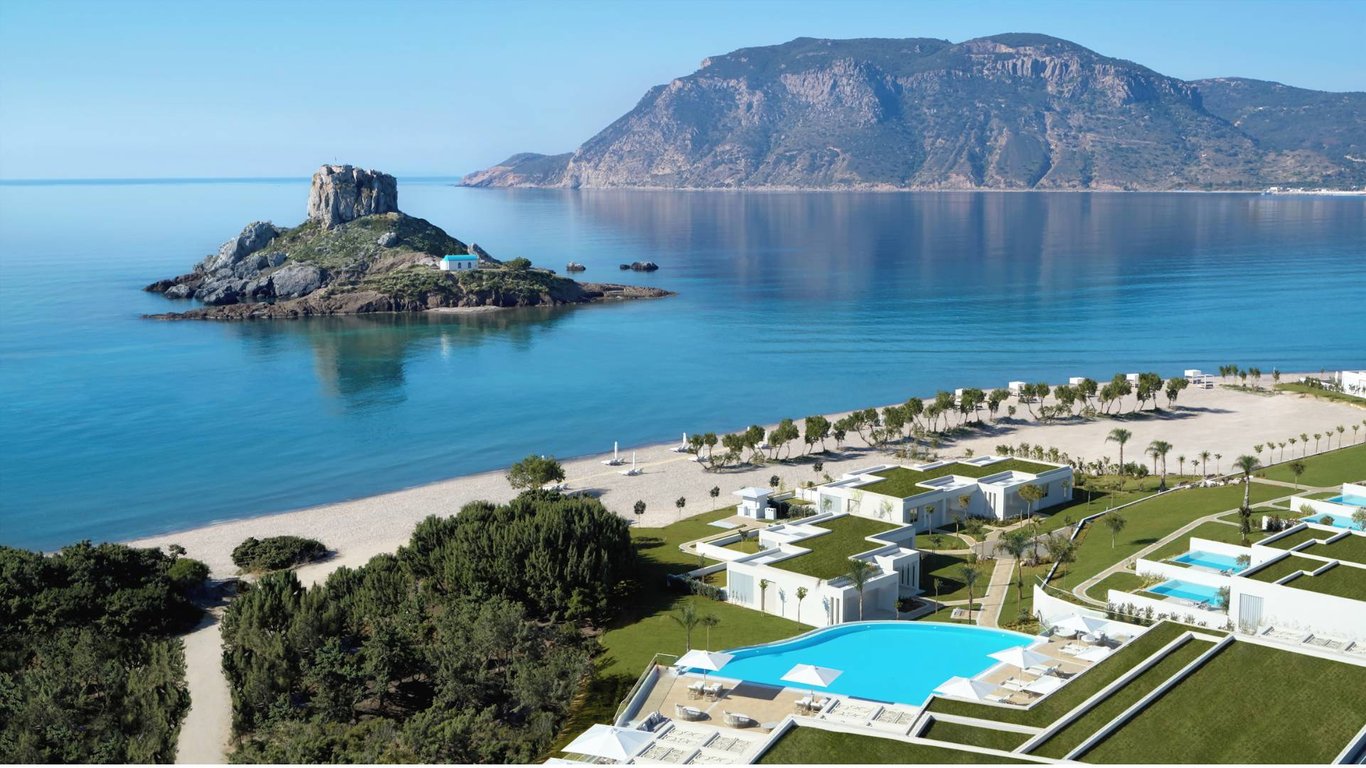 Aerial view of Ikos Aria resort in Kos, Greece, with contemporary white buildings, a pool, greenery, and the Aegean Sea.