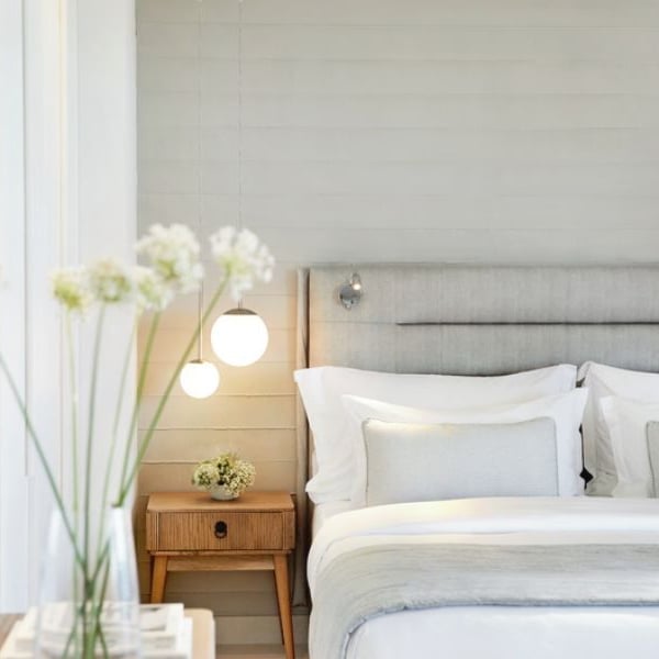 Elegant bedroom at Ikos Aria hotel with a double bed, light grey linens, a wooden nightstand, soft ambient lighting, and a mirror.