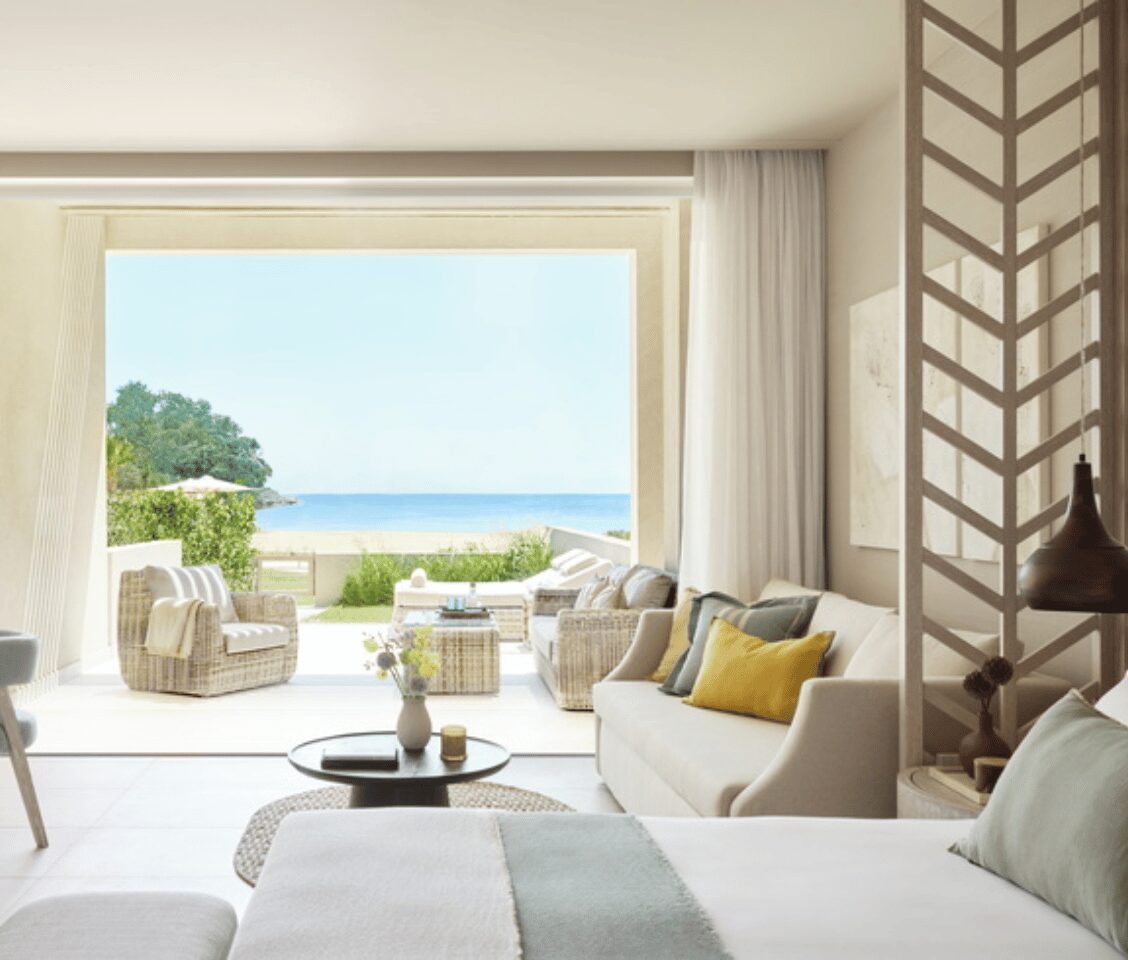 Deluxe Junior Bungalow Suite at Ikos Odisia, featuring a private garden and sea view through large sliding doors, with elegant interior seating and decor in soft colours.