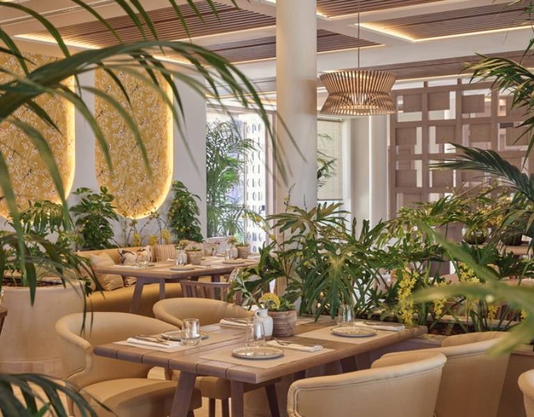 Indoor restaurant at Ikos Odisia resort with elegantly set tables, lush greenery, and modern lighting.