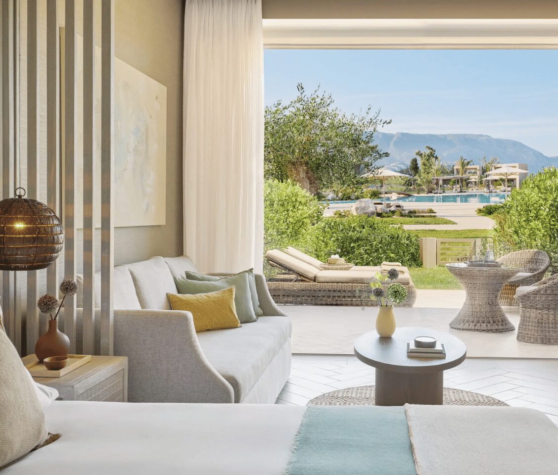 Ikos Odisia junior suite with a private garden, featuring a modern interior, outdoor seating, and a view of the pool.