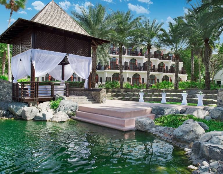 Amphitheatre at JA Palm Tree Court in Dubai, featuring a gazebo with white curtains, surrounded by a water feature and lush gardens with palm trees.