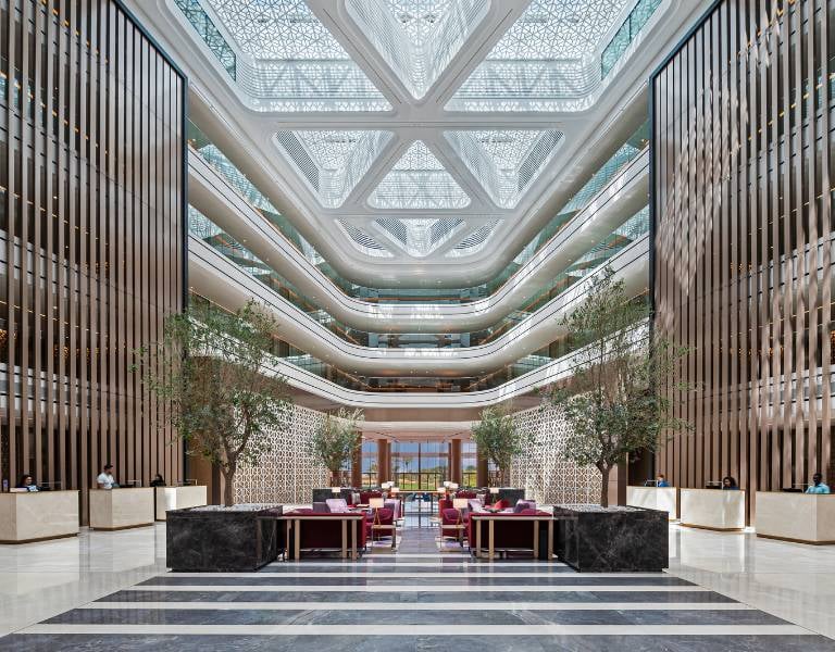Luxurious lobby of JA Gallery with high ceiling, marble floors, stylish seating, and decorative greenery.