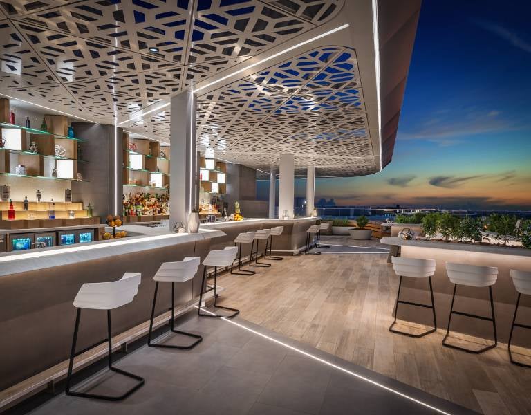 Outdoor bar at JA Gallery with modern seating, ambient lighting, and a scenic sunset view of the city.