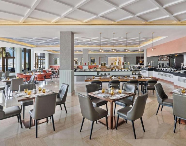 Elegant restaurant interior with a large dining area, contemporary decor, neatly set tables, and a buffet counter in the background.
