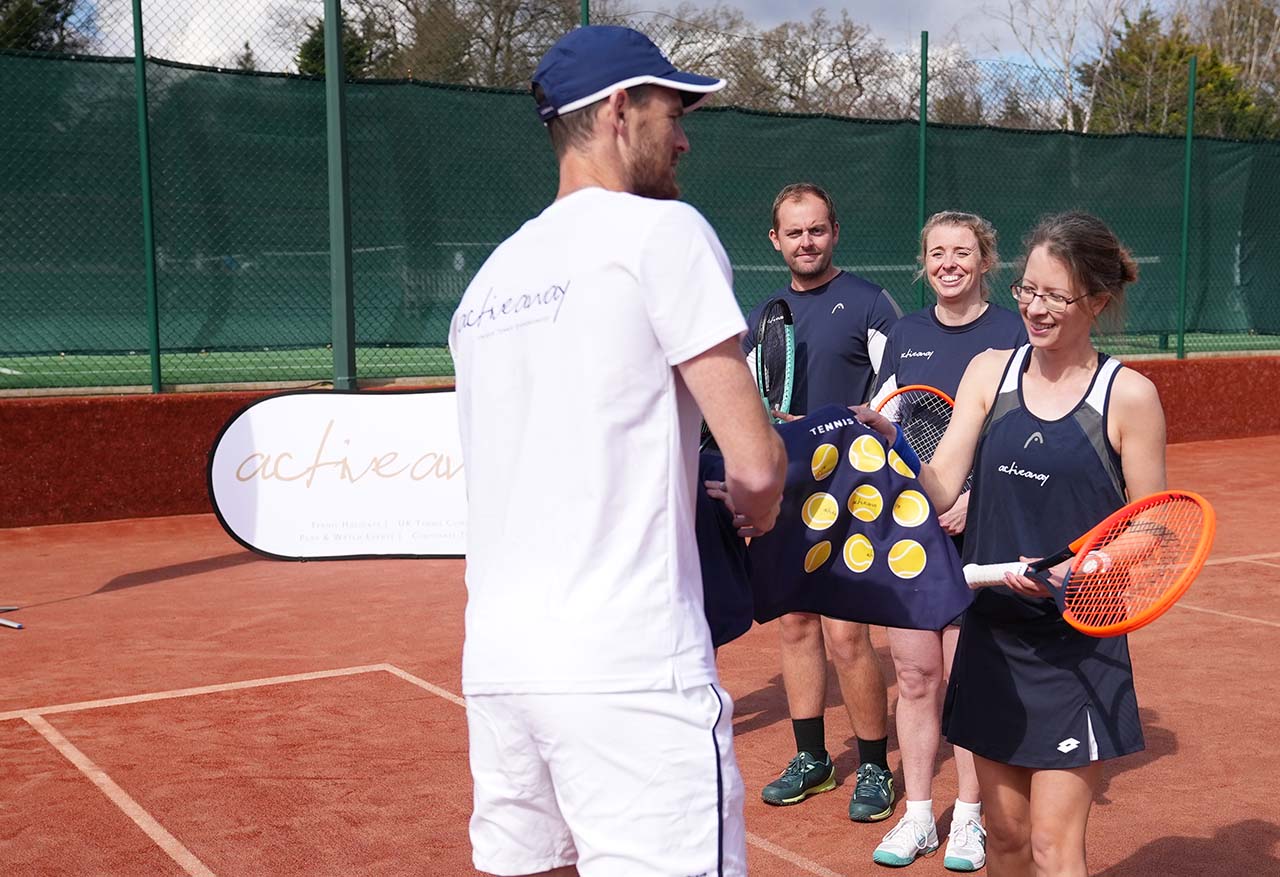 Jamie Murray on a tennis court, interacting with two women and a man holding tennis equipment.