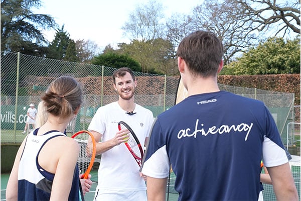 Jamie Murray with the Active Away team on a tennis court, engaging with two tennis players.