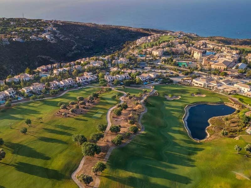 Aerial view of Aphrodite Hills Resort with golf course and villas, set against an ocean backdrop.