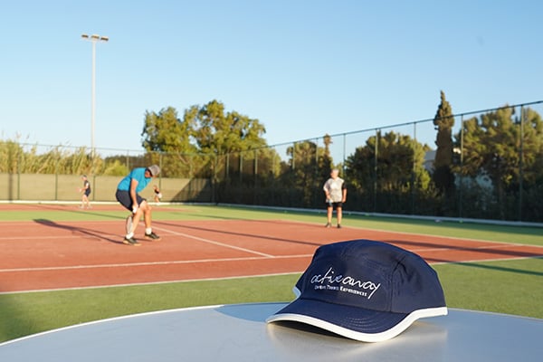 Active Away cap on a table in front of a tennis court with players in the background.
